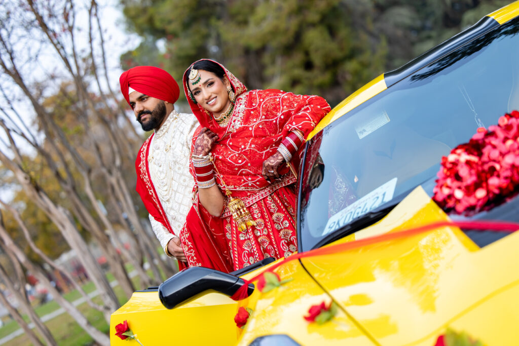 Sikh bride and groom (Jass & Vickey) posing next to a bright yellow decorated sports car on their wedding day.